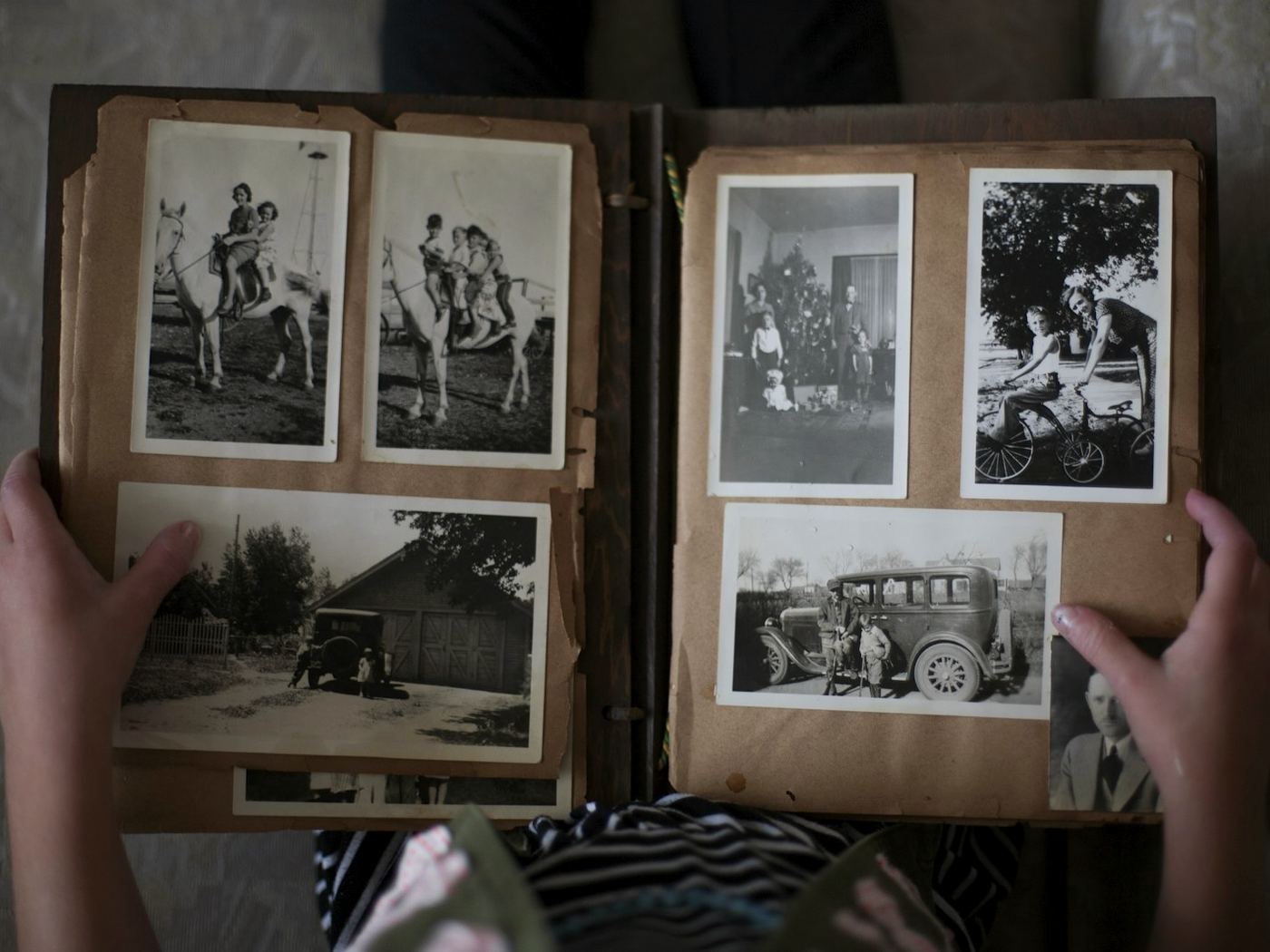 Iemand houdt een oud familiealbum open op schoot; de pagina's staan vol zwart-witfoto's